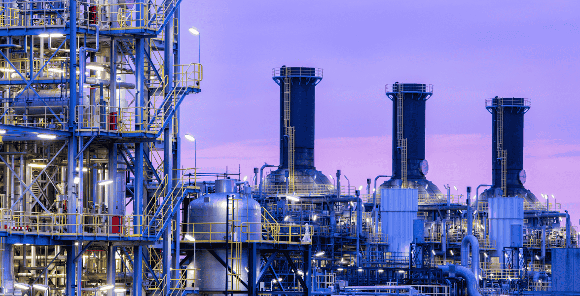 Close-up of industrial refinery structures with pipelines and towers at dusk, featuring clear purple sky.