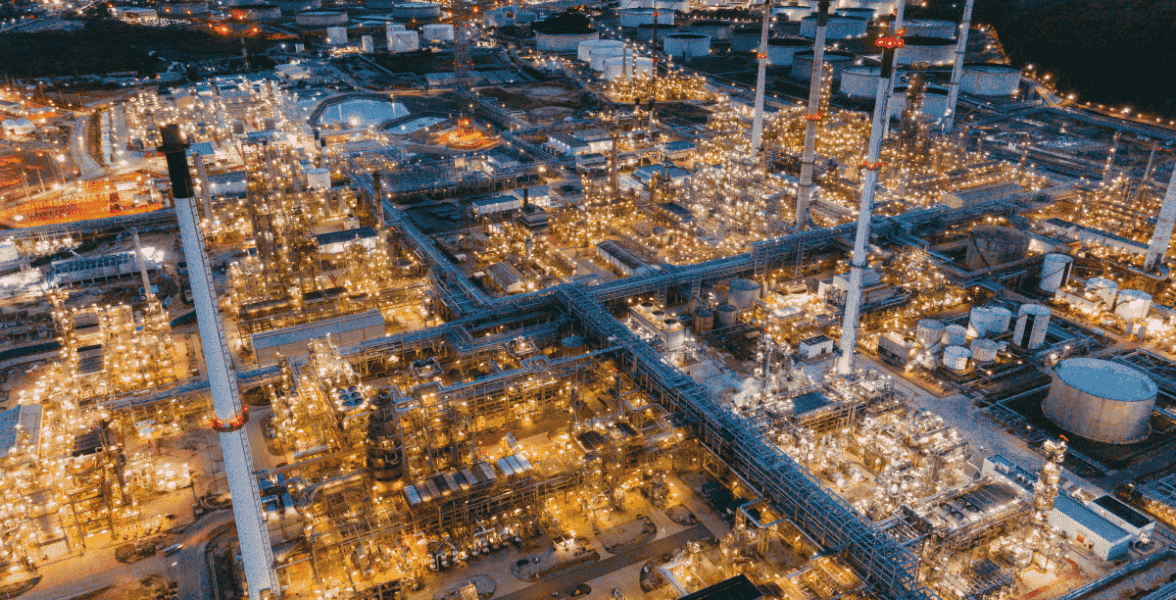 Wide-angle nighttime view of a vast, illuminated oil refinery or chemical plant with complex infrastructure.