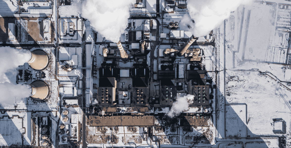 Aerial view of a large power plant with cooling towers emitting steam during winter conditions.